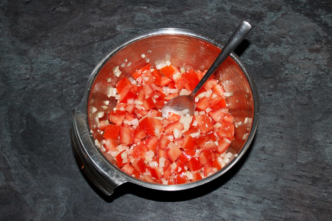 Diced desseded tomato, diced onion and garlic mixed together in a silver bowl