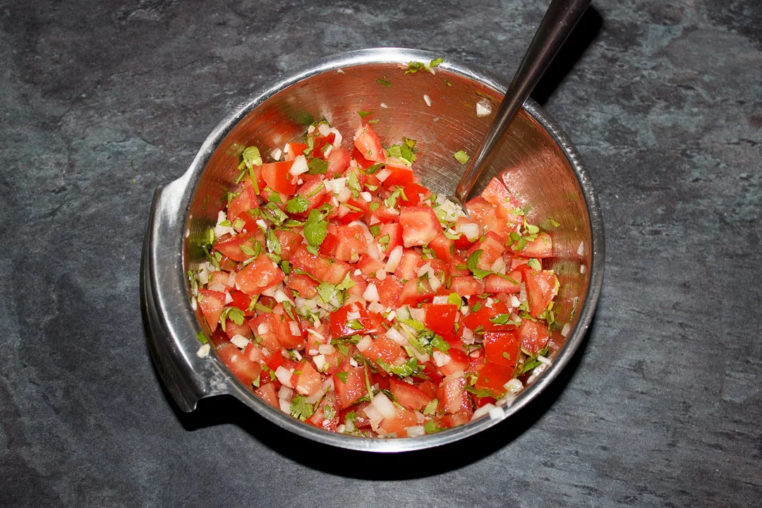 Diced desseded tomato, diced onion, garlic and coriander mixed together in a silver bowl