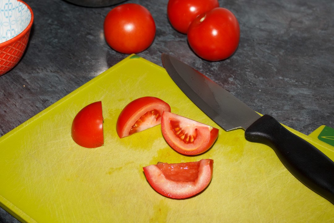 A quartered tomato on a green chopping board with a sharp knife