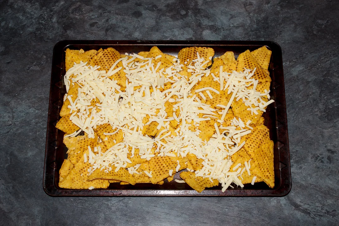 Tortilla chips spread out on a baking tray covered in grated cheese
