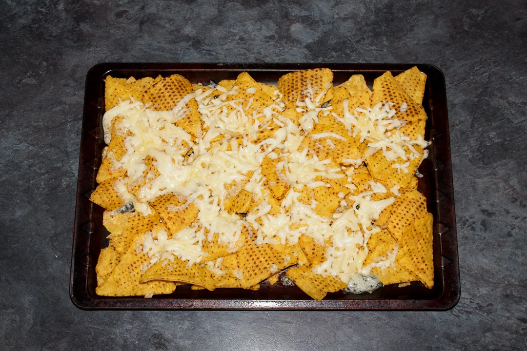 Tortilla chips spread out on a baking tray covered in melted cheese