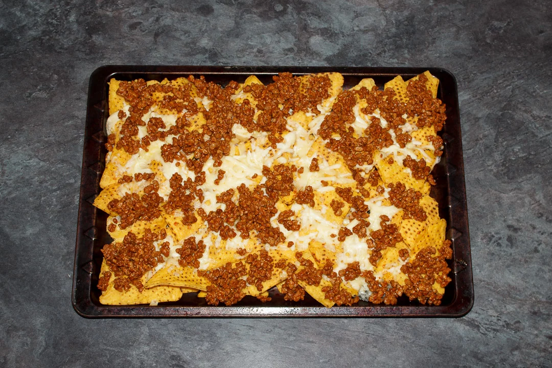 Tortilla chips spread out on a baking tray covered in melted cheese and taco seasoned soya mince