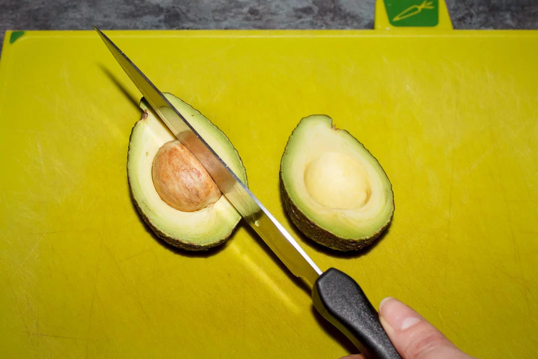 a knife cutting into an avocado stone on a green chopping board