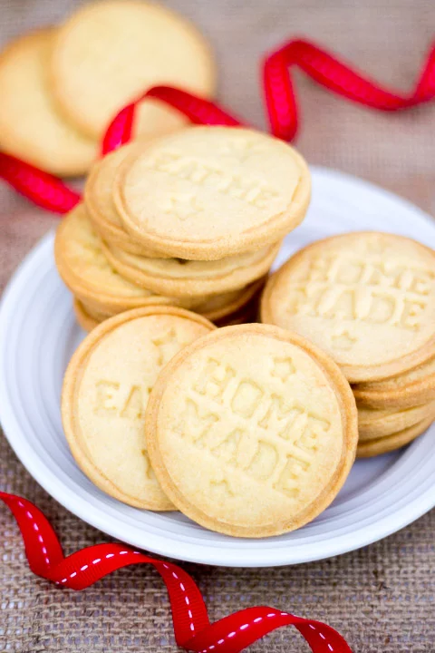 Butter biscuits piled up on a white plate with red ribbon curled around it