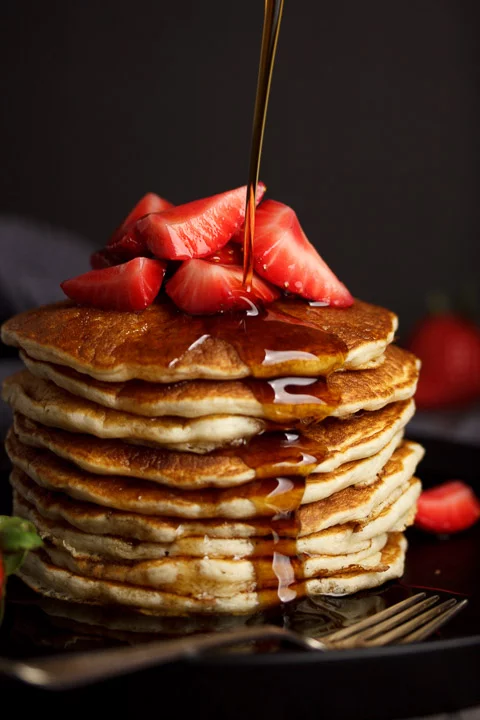 Fluffy vegan American pancakes in a stack topped with strawberries and maple syrup