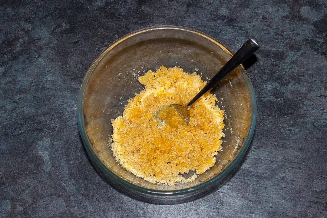 Sugar and egg yolks mixed together in a glass bowl with a spoon
