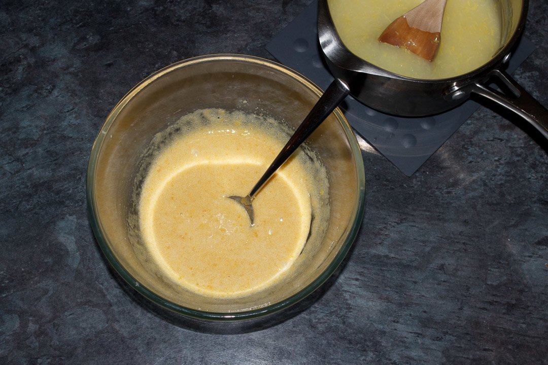 Sugar, egg yolks and some of the lemon mixture mixed together in a glass bowl with a spoon