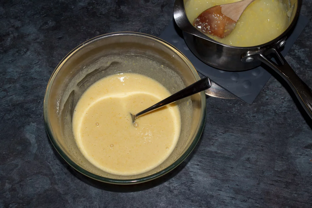 Sugar, egg yolks and some of the lemon mixture mixed together in a glass bowl with a spoon