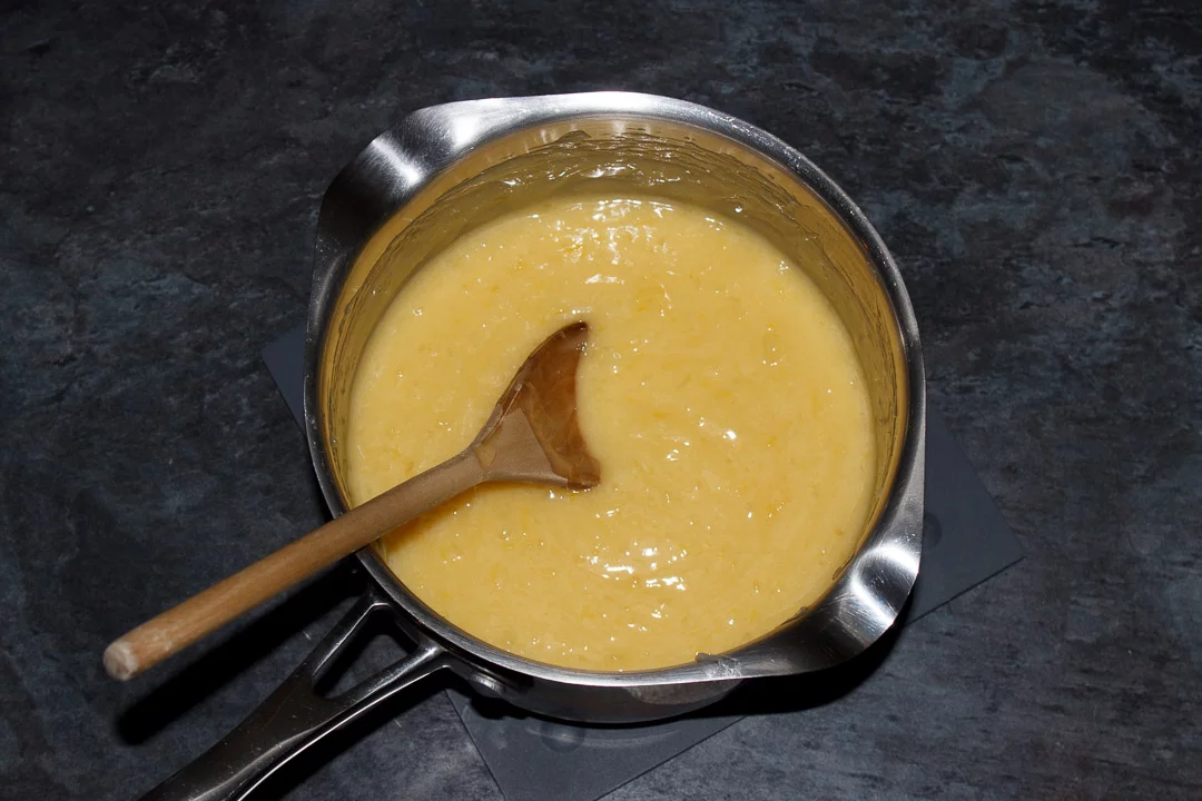 Lemon meringue pie filling in a saucepan with a wooden spoon