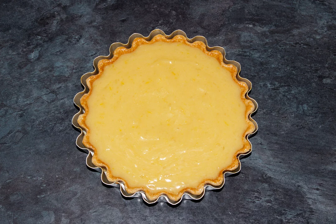A shortcrust pastry case in a tart tin filled with a lemon curd filling