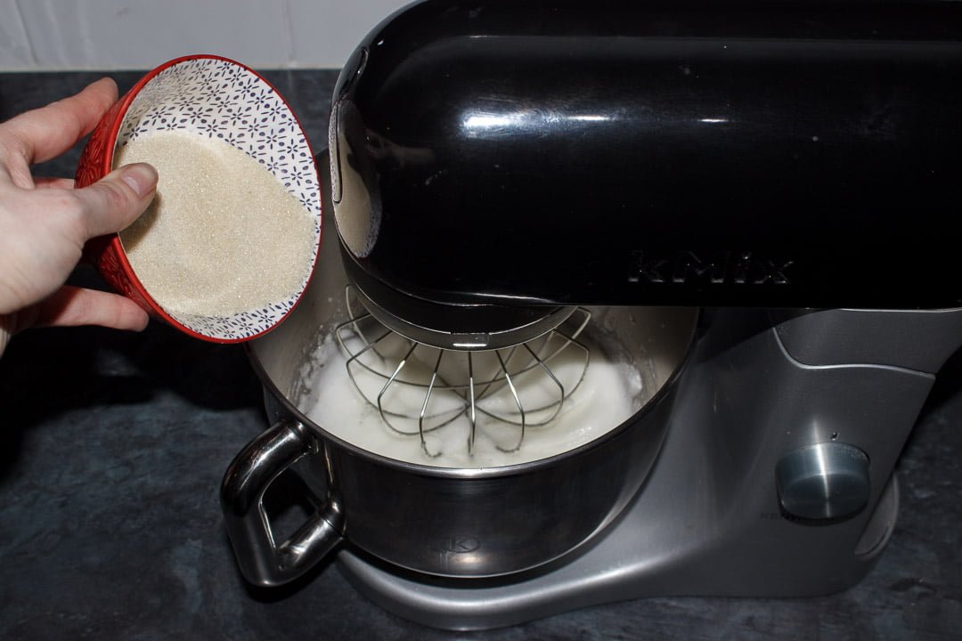Sugar being added to whipped egg whites in an electric stand mixer