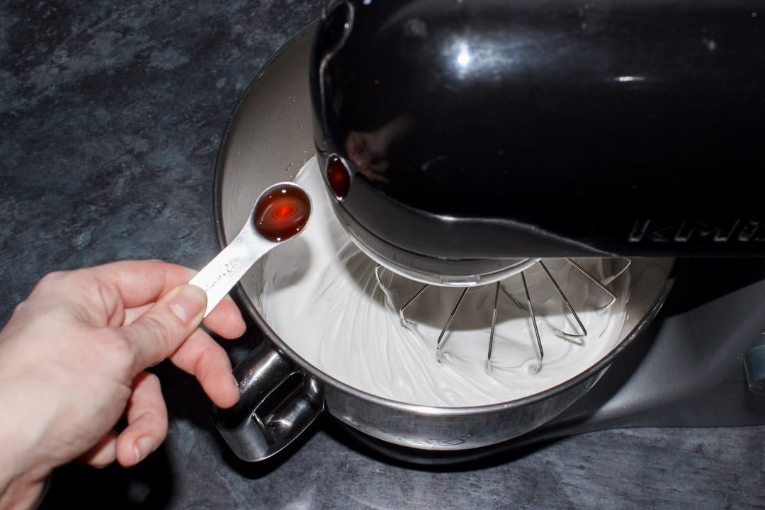 Vanilla being added to whipped egg whites in an electric stand mixer