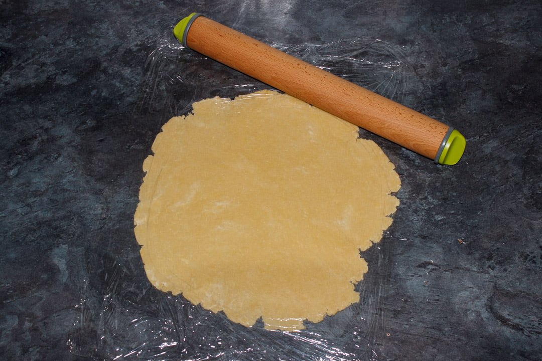 Shortcrust pastry dough rolled out on a piece of cling film with a rolling pin