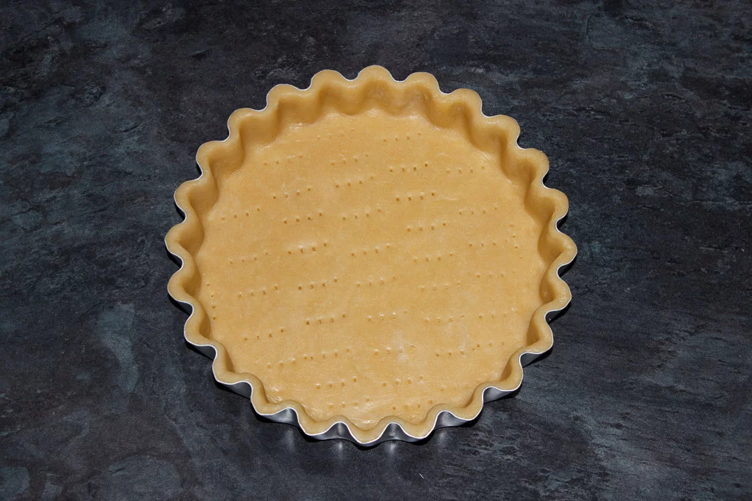 A tart tin lined with shortcrust pastry that's been pricked with a fork