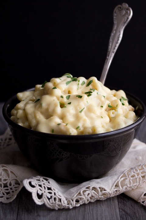 Macaroni cheese in a black bowl topped with fresh parsley