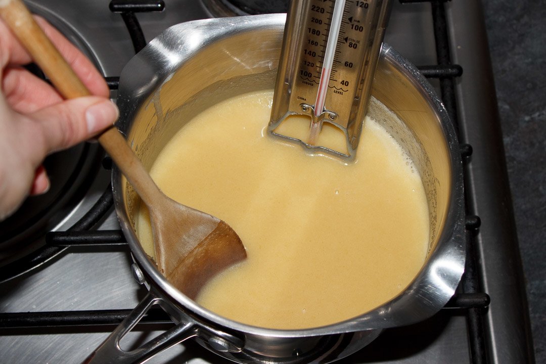 Pale caramel being stirred in a medium sized saucepan over a low heat with a thermometer