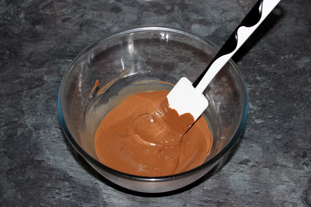 Melted milk chocolate in a glass bowl with a white spatula