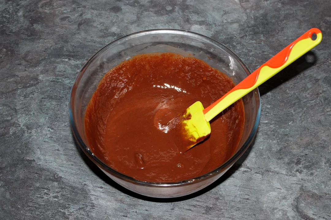 Dark chocolate, butter and eggs mixed together in a glass bowl with a green spatula
