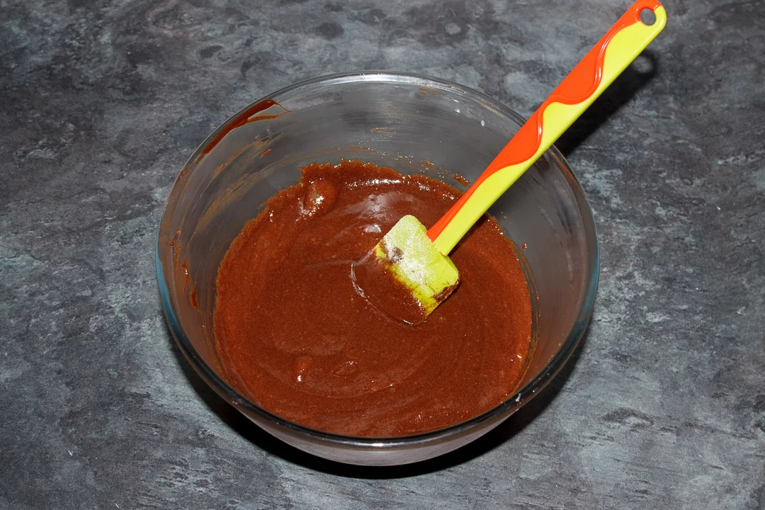 Dark chocolate, butter, eggs and caster sugar mixed together in a glass bowl with a green spatula