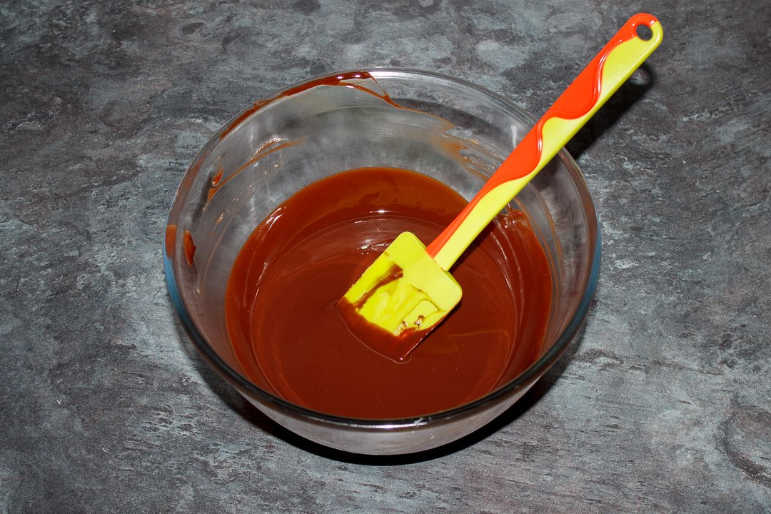 Dark chocolate and butter melted in a glass bowl with a green spatula