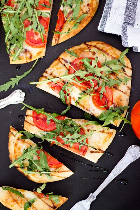 Sliced naan bread pizza topped with tomato and rocket