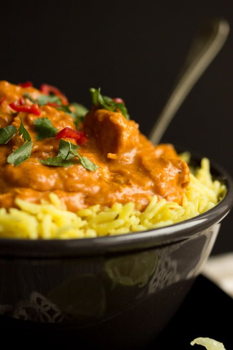 Slow cooker chicken curry in a black bowl with pilau rice