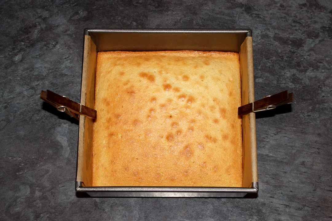 A baked lemon traybake cake cooling in a square tin