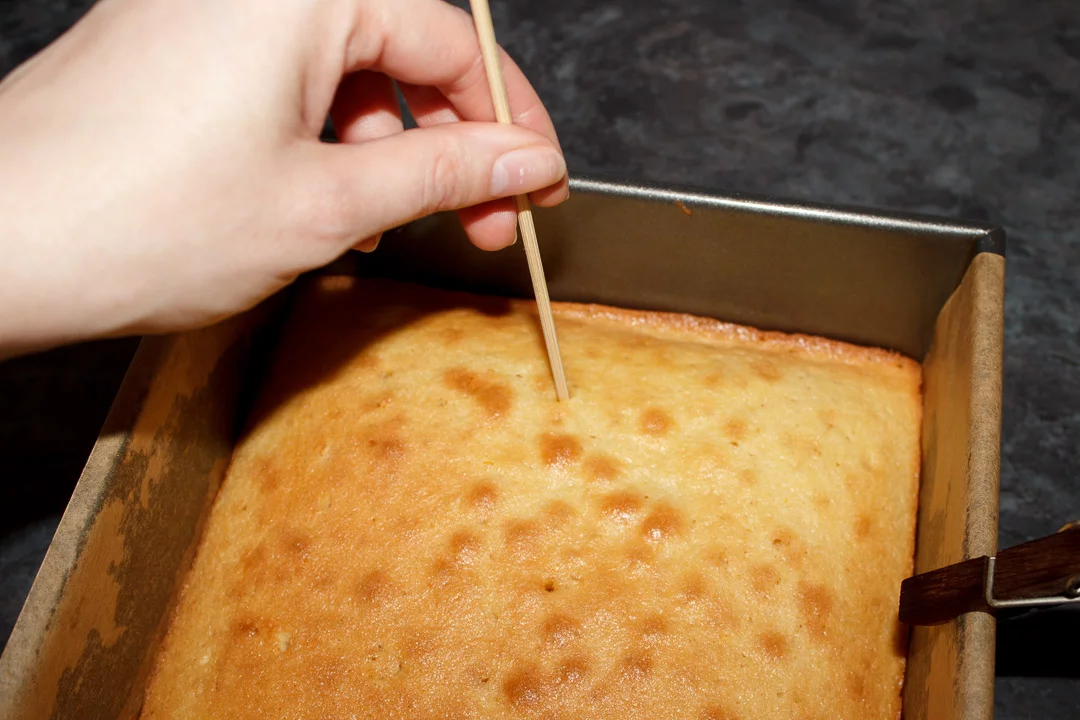 A lemon traybake cake being poked all over with a skewer