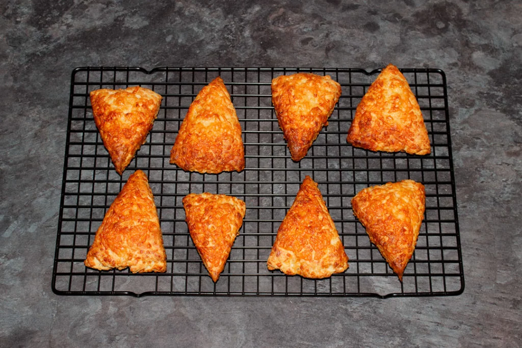 Freshly baked cheese scones on a wire cooling rack.