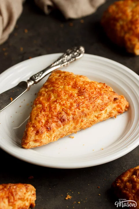 A cheese scones and knife on a white plate, with other cheese scones surrounding it.
