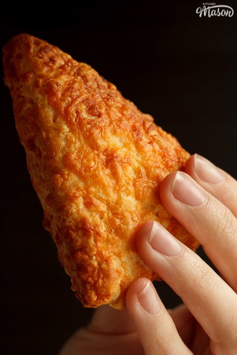 A cheese scone being held against a black background