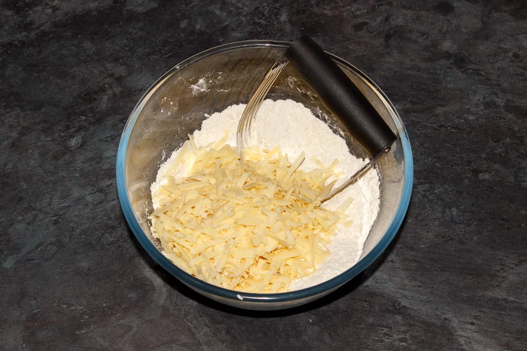 Flour, butter and grated cheese in a bowl with a pastry whisk