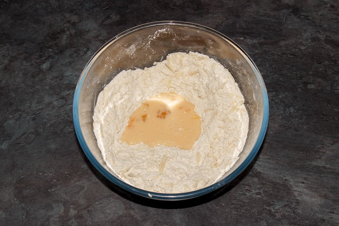 Cheese scones dry ingredients in a bowl with egg and milk in a well in the middle and a pastry whisk