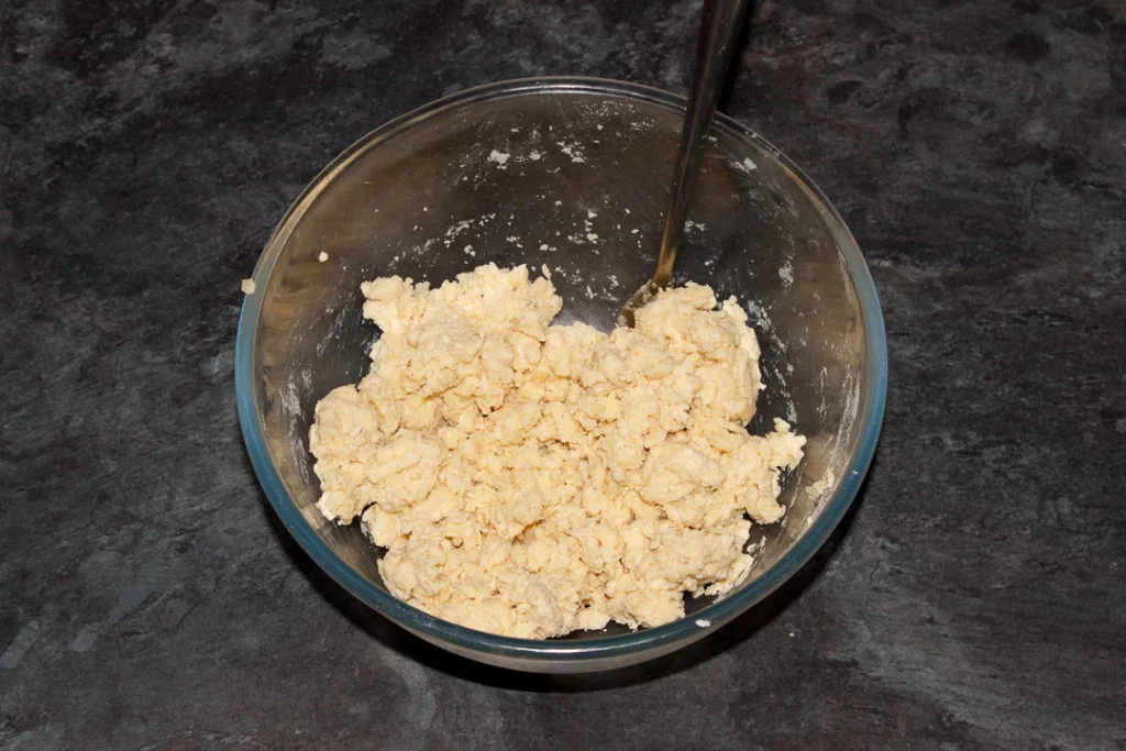 Cheese scones dough in a large mixing bowl with a fork.