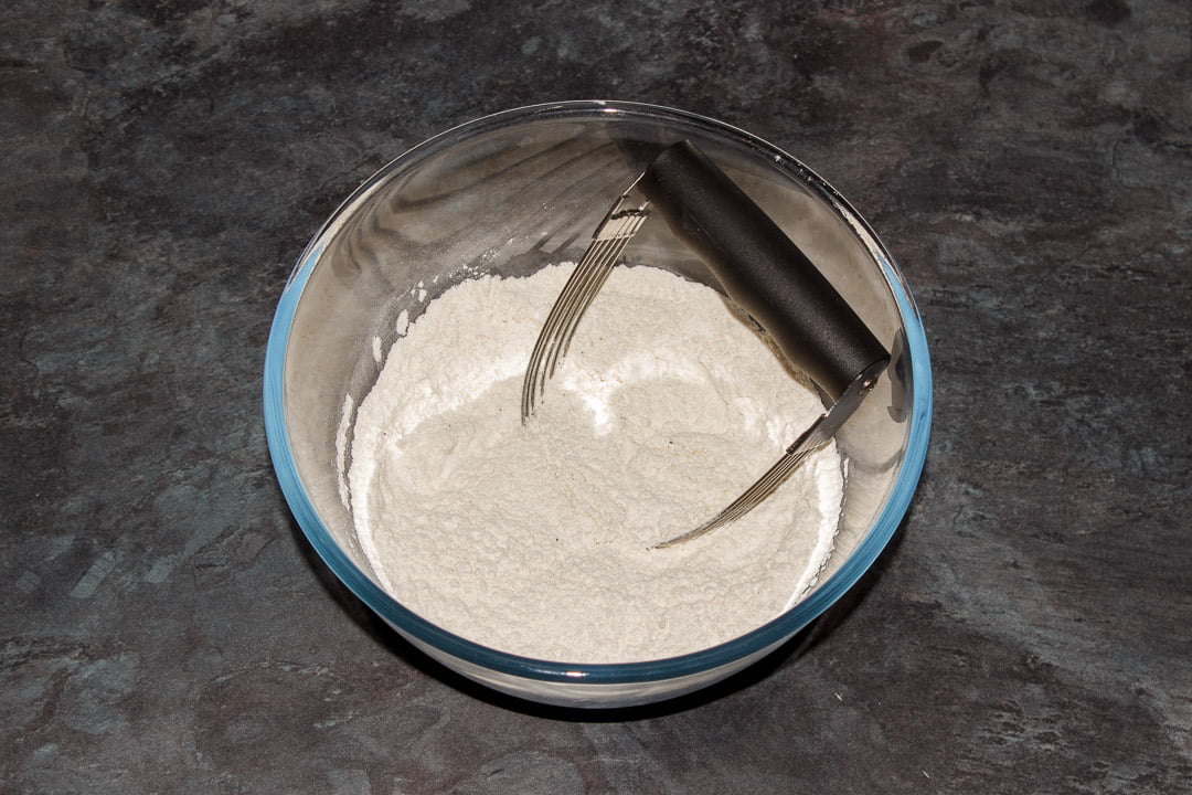 Flour, baking powder and seasoning in a bowl with a pastry whisk