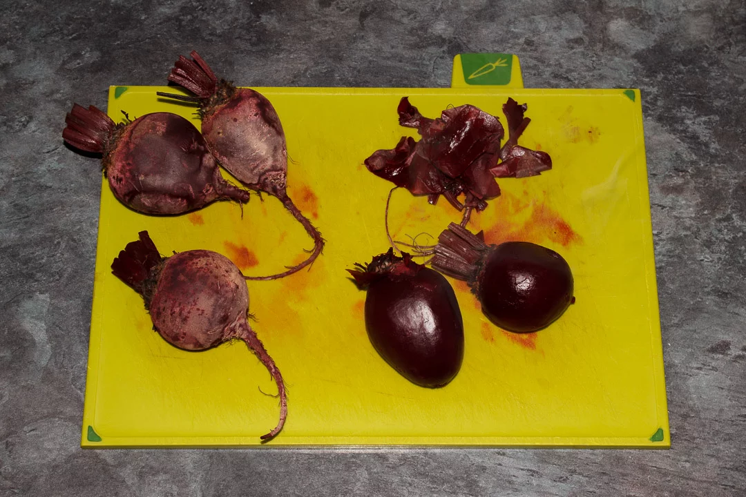 Whole beetroot having their skins peeled off on a chopping board