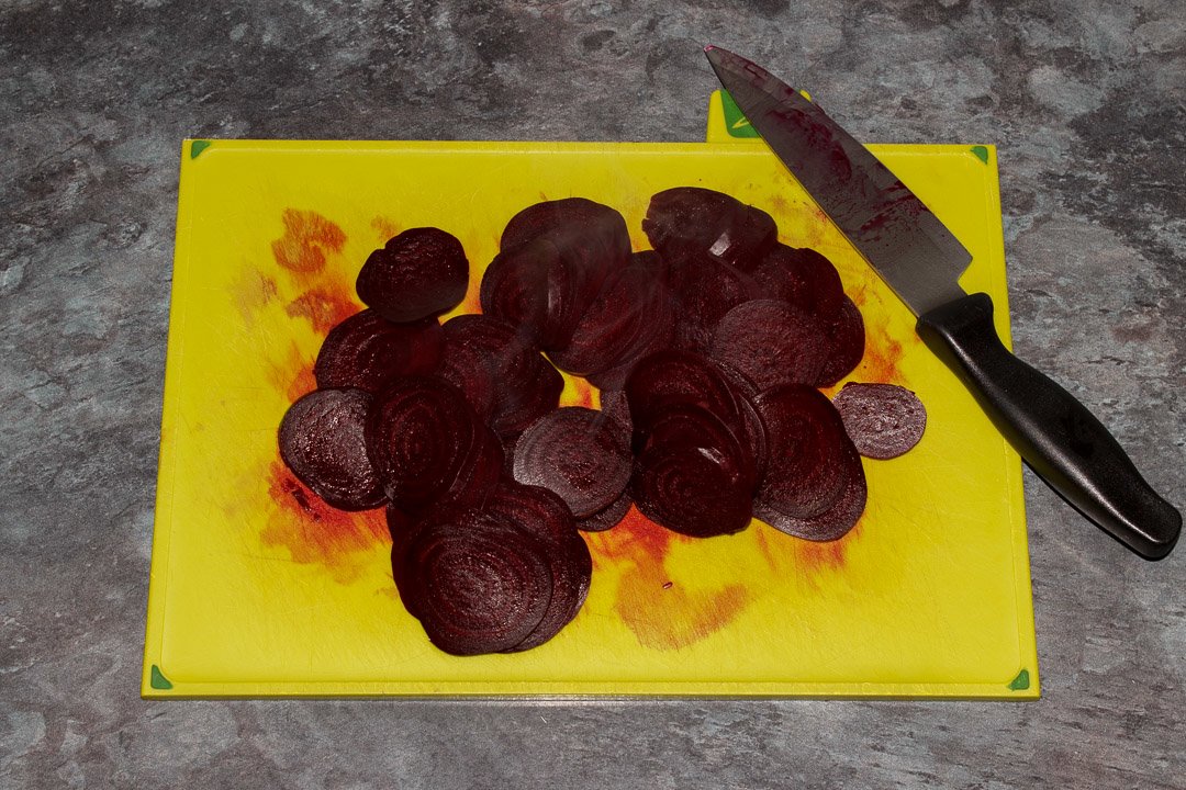 Sliced cooked beetroot on a chopping board with a sharp knife