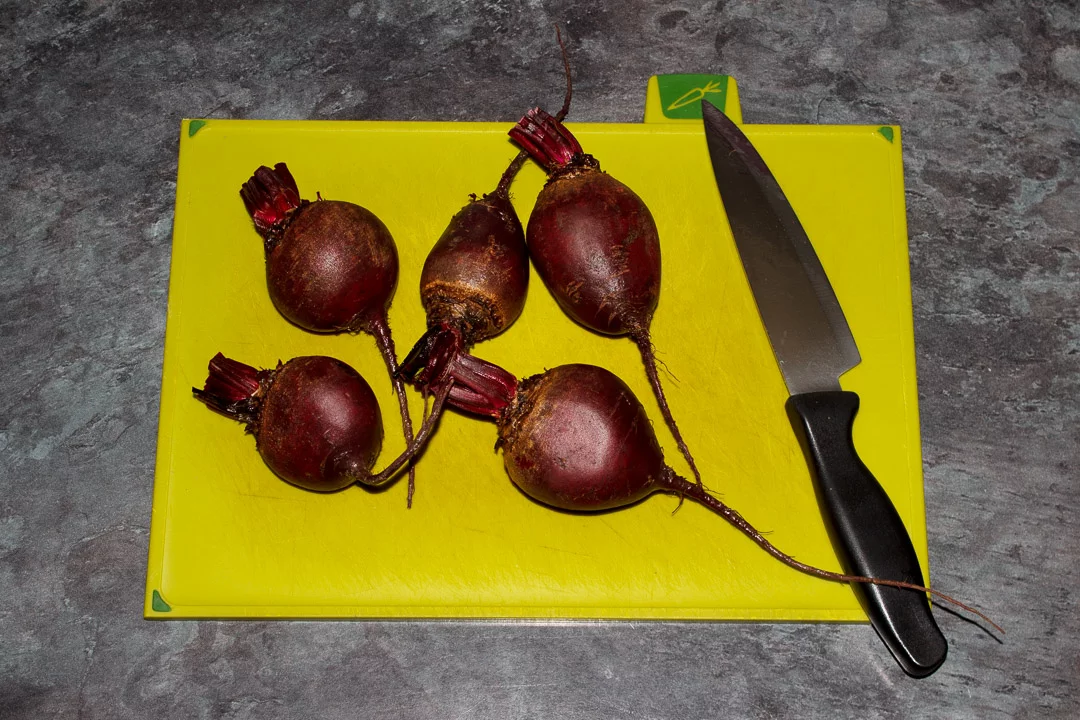 Washed whole beetroot with the stems trimmed on a chopping board with a knife
