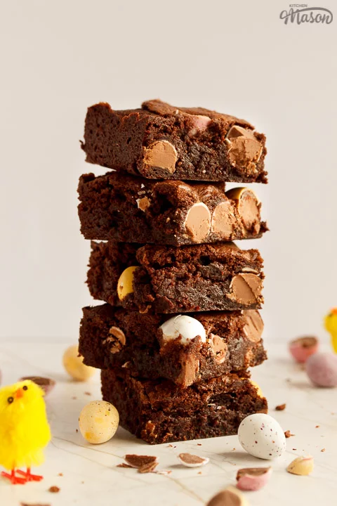 A stack of 5 Mini Egg brownies surrounded by broken Mini Eggs and Easter chicks