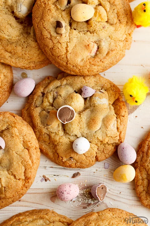 Mini Egg cookies in a pile on a worktop alongside scattered Mini Eggs and little yellow chicks