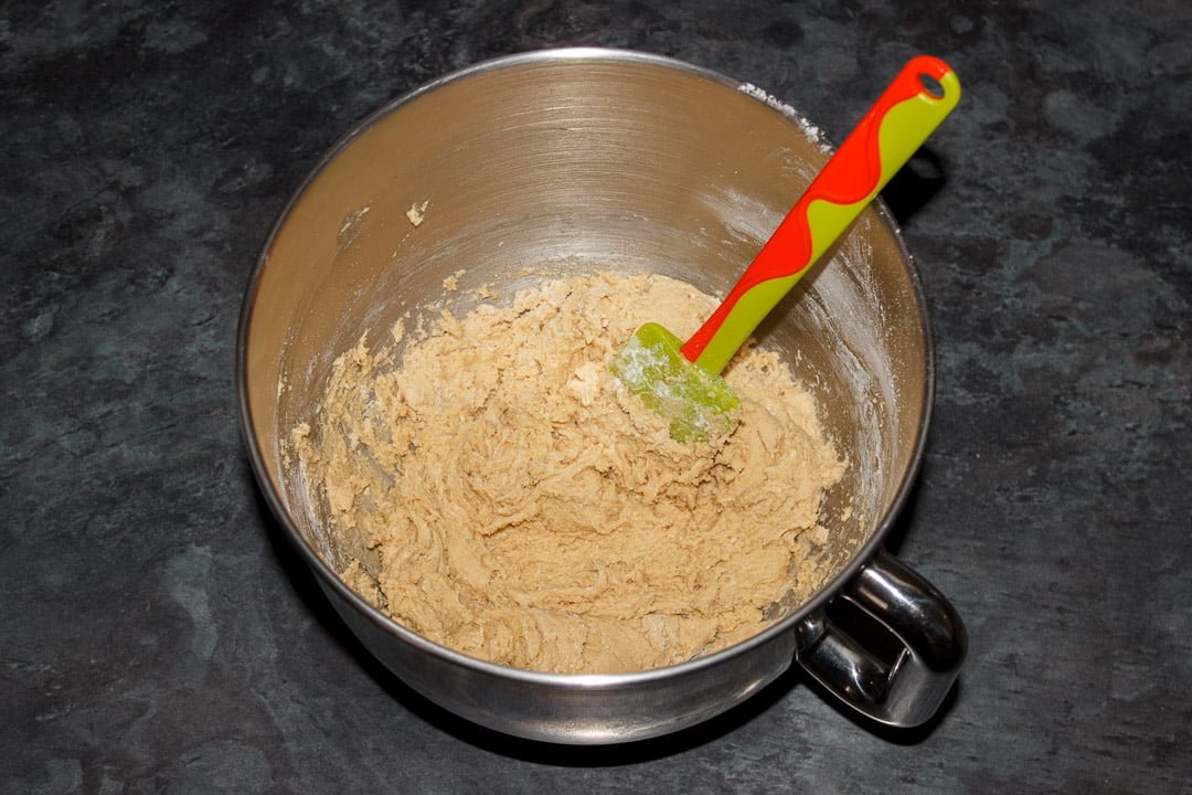 Cookie dough in a large bowl with a green and orange rubber spatula