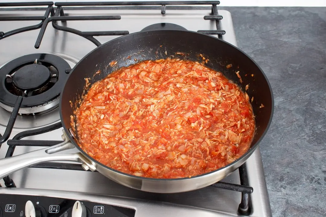 A tuna pasta bake sauce and tuna simmering in a large frying pan on a hob