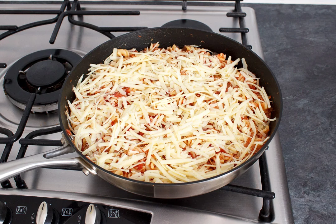 Tuna pasta bake topped with grated cheese in a large frying pan on a hob