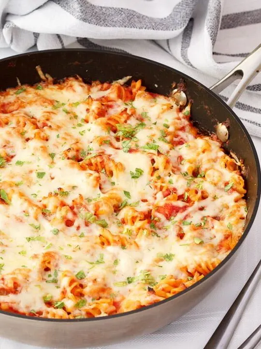 Tuna pasta bake in a large frying pan on a white table cloth with two silver forks