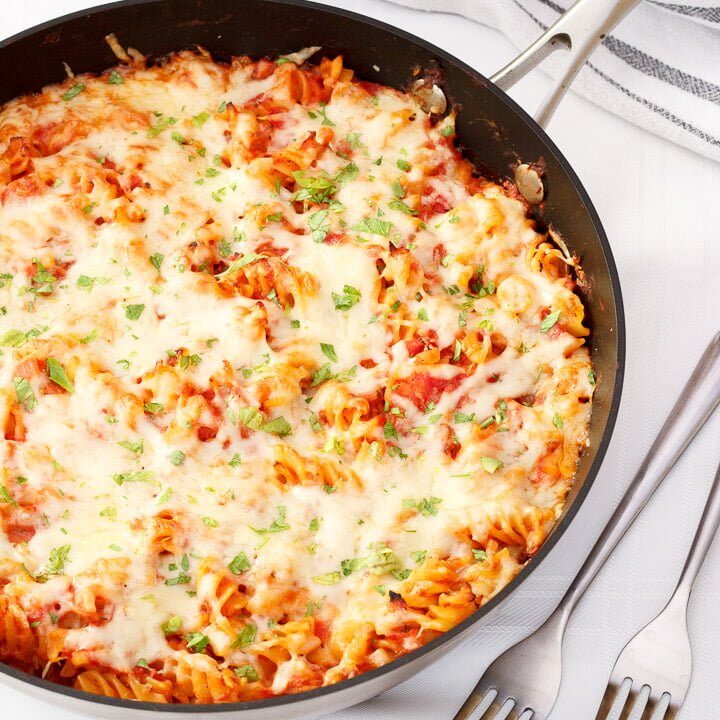 Tuna pasta bake in a large frying pan on a white table cloth with two silver forks