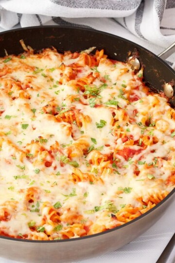 Tuna pasta bake in a large frying pan on a white table cloth with two silver forks