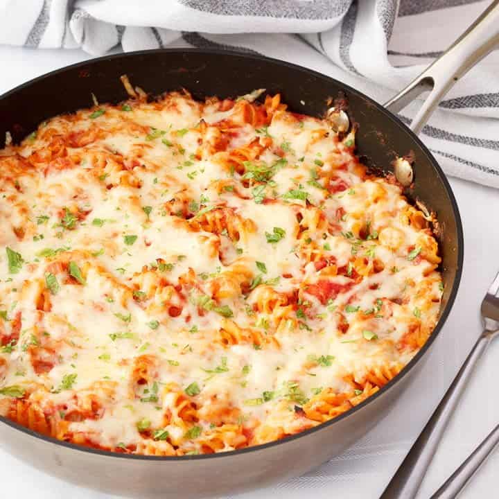 Tuna pasta bake in a large frying pan on a white table cloth with two silver forks
