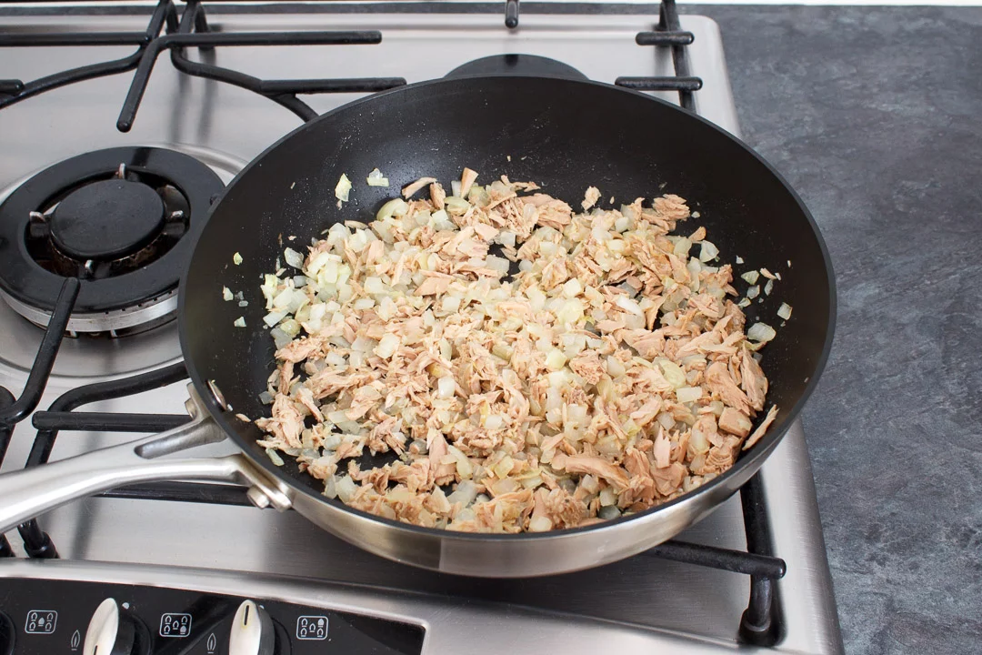 Tuna, onion and garlic cooking in a large frying pan on a hob