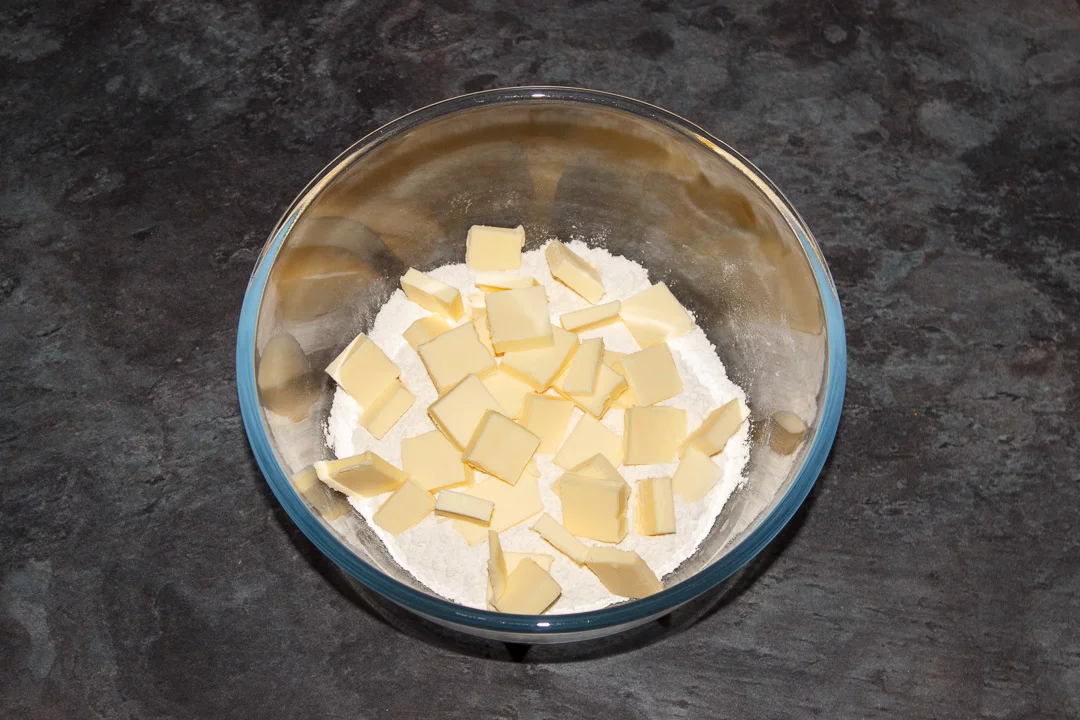 Flour and salt in a large glass bowl with cubed cold butter on top
