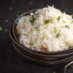 freshly cooked rice scattered with chopped coriander in the top bowl of a stack of 3 with a fork next to it